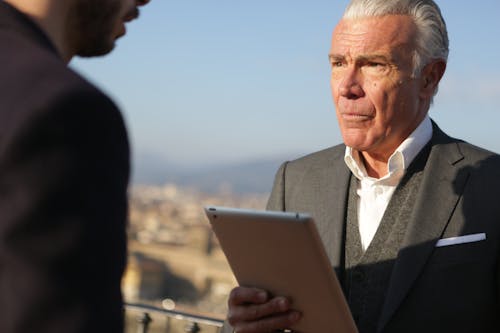 Man in Black Suit  Holding Silver Ipad Looking at Another Man