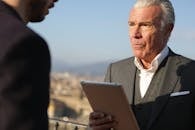 一位老年男子在户外商务环境中专注地使用着平板电脑