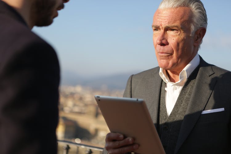 Man In Black Suit  Holding Silver Ipad Looking At Another Man