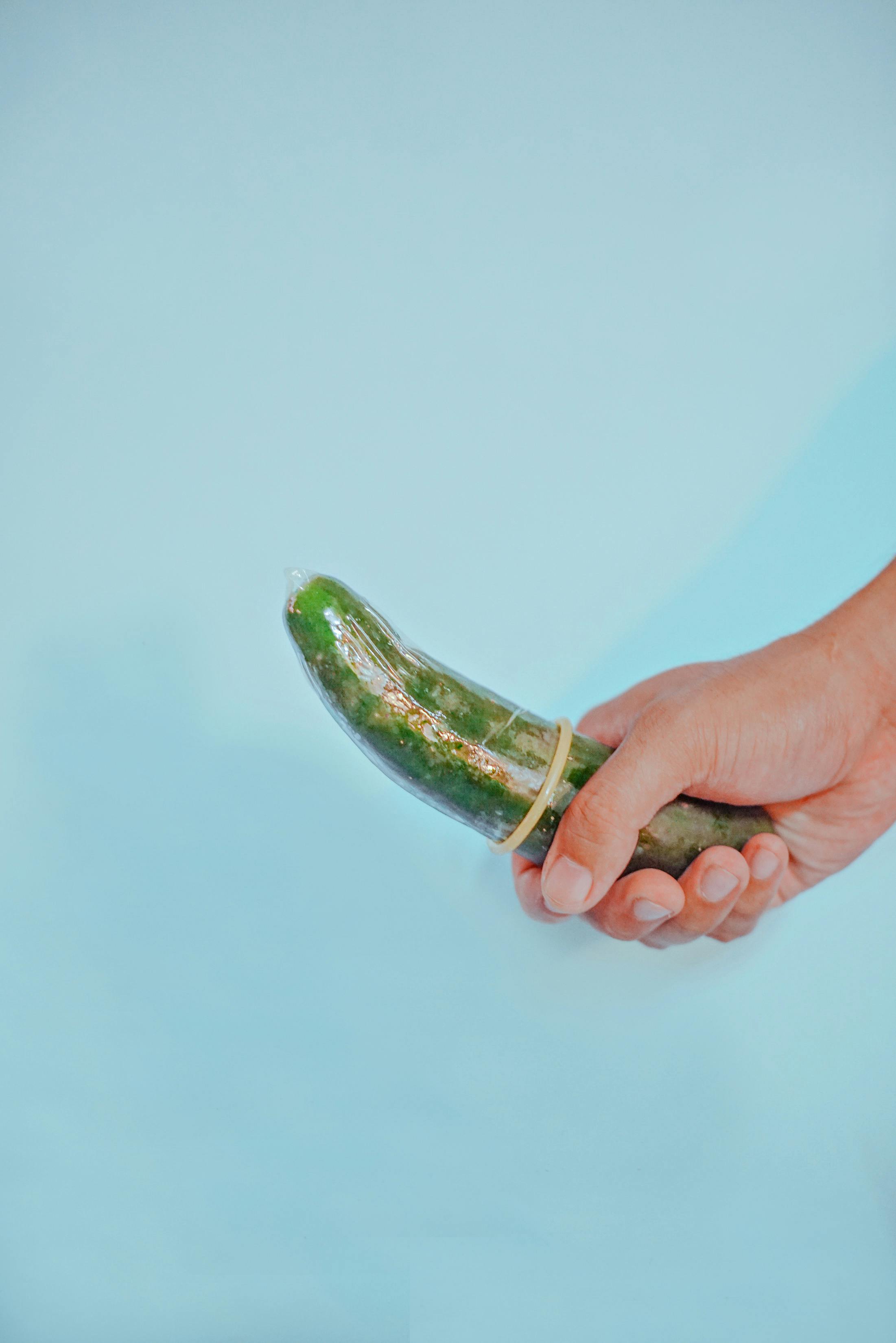 a person holding a cucumber with condom