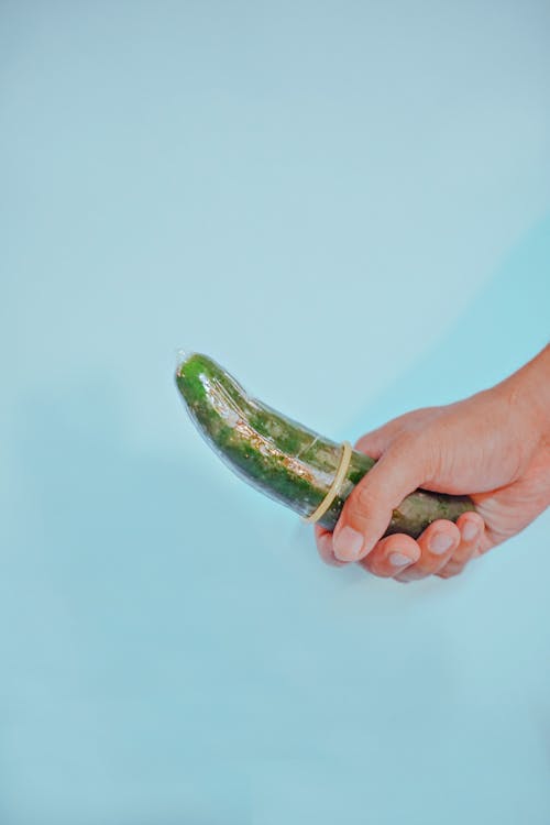 Free A Person Holding a Cucumber with Condom Stock Photo