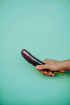 Close-up of a hand holding an eggplant against a solid green background. — photo by FounderTips .