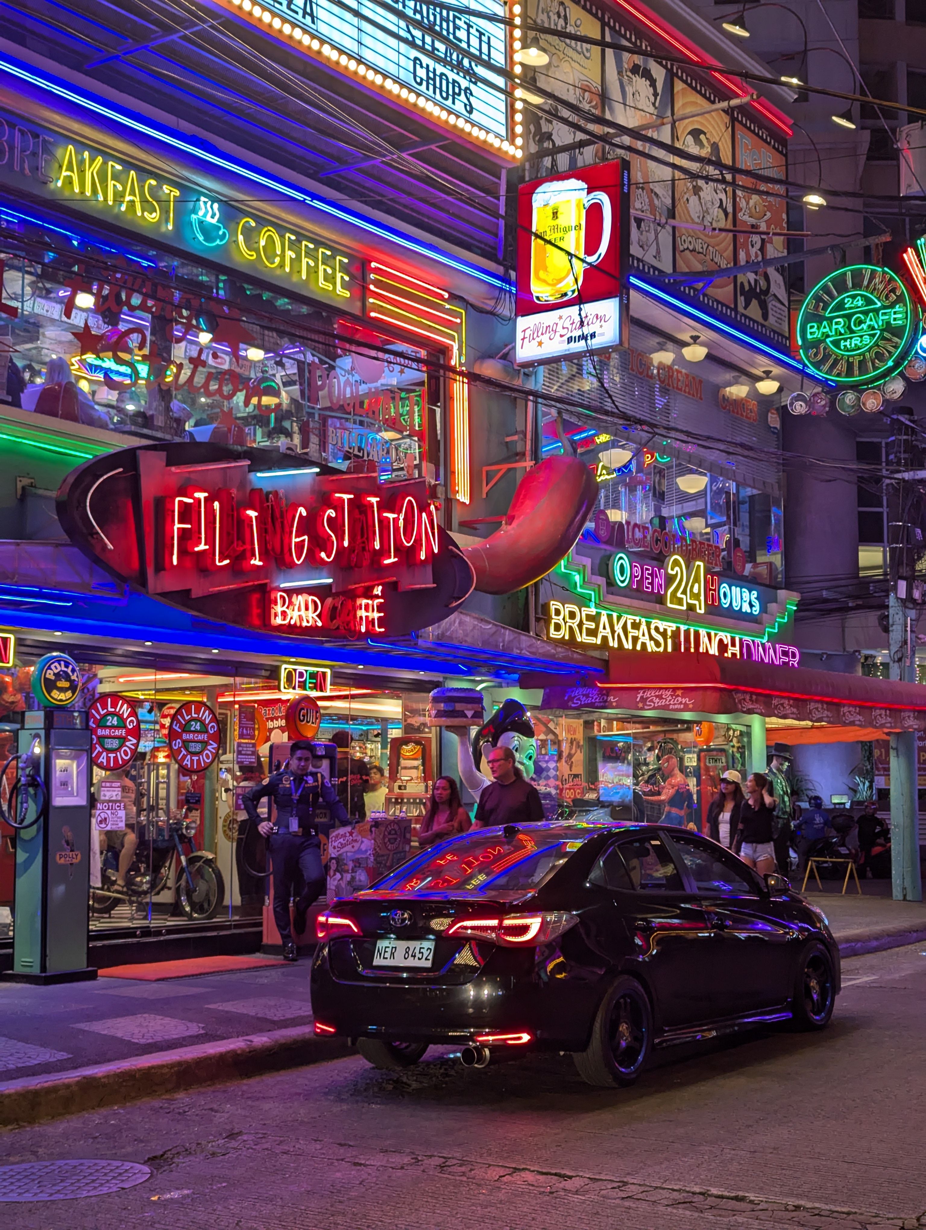 Lively city evening with colorful neon signs, people, and a car at a bustling diner.