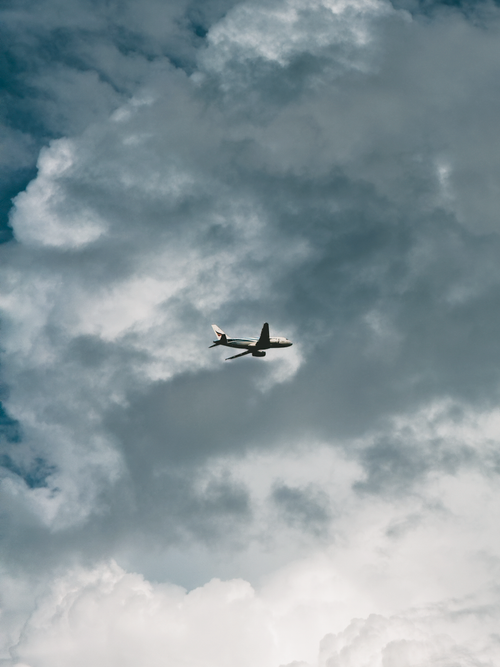 Free Airplane soaring through large dramatic clouds on a bright day, symbolizing travel and freedom. Stock Photo