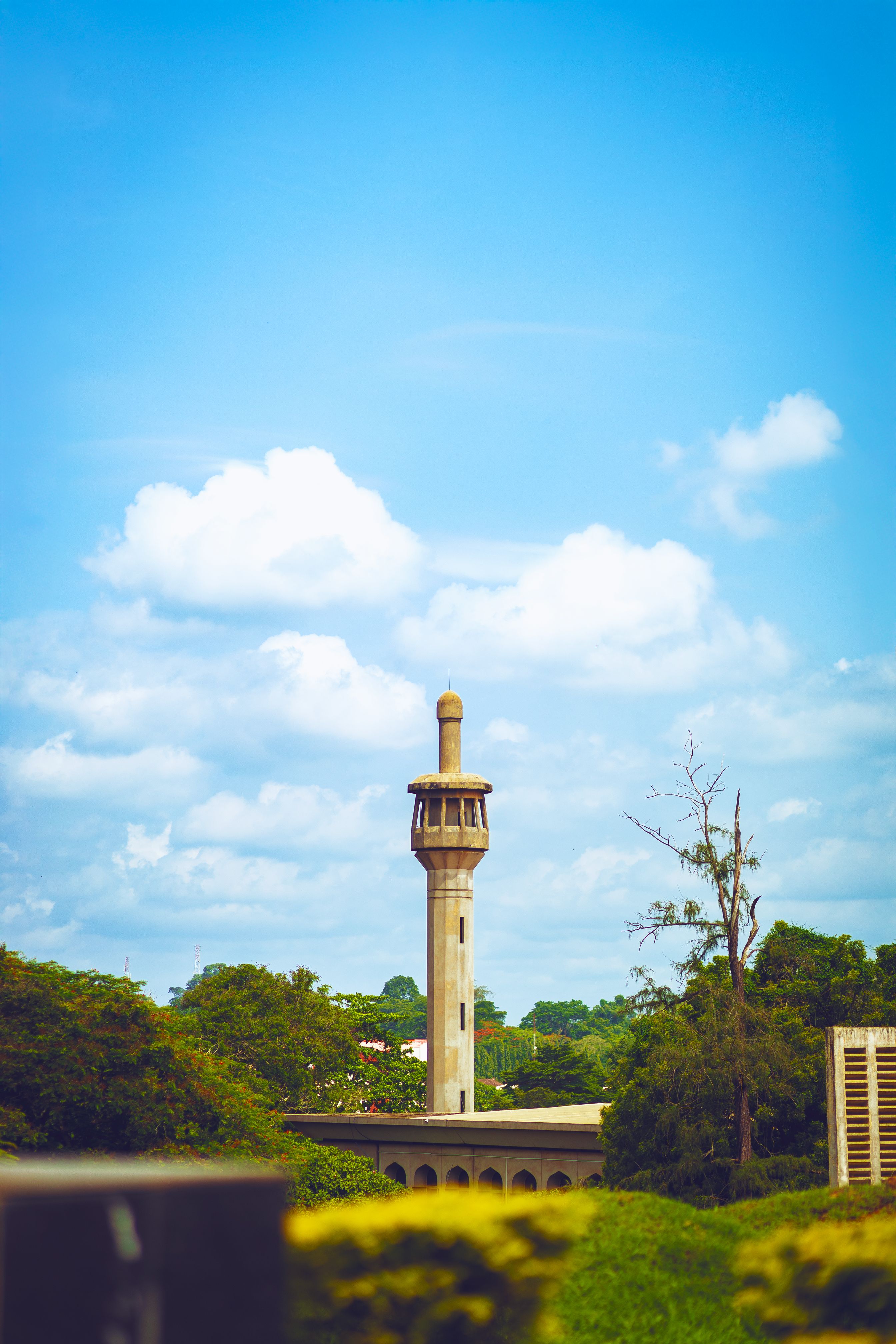 A beautiful mosque minaret surrounded by greenery under a bright blue sky in Ibadan, Nigeria.