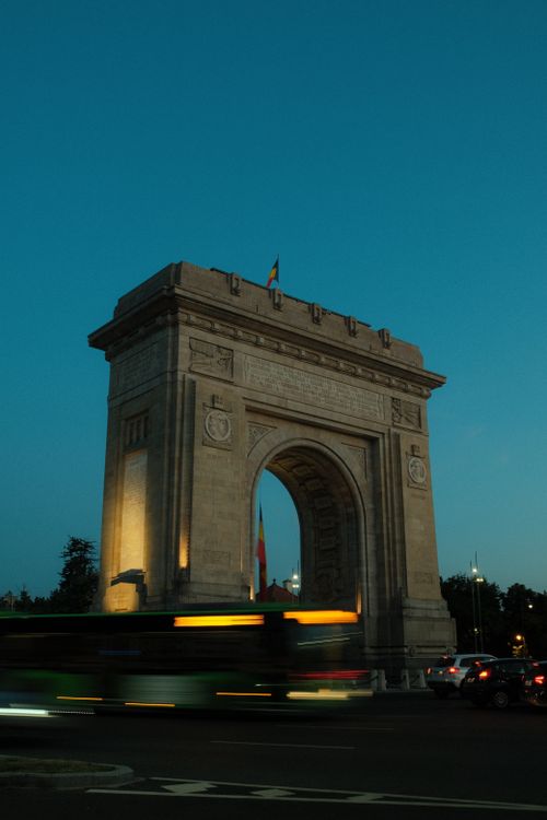 Free Stunning view of Bucharest's Arcul de Triumf illuminated at dusk with urban traffic passing. Stock Photo