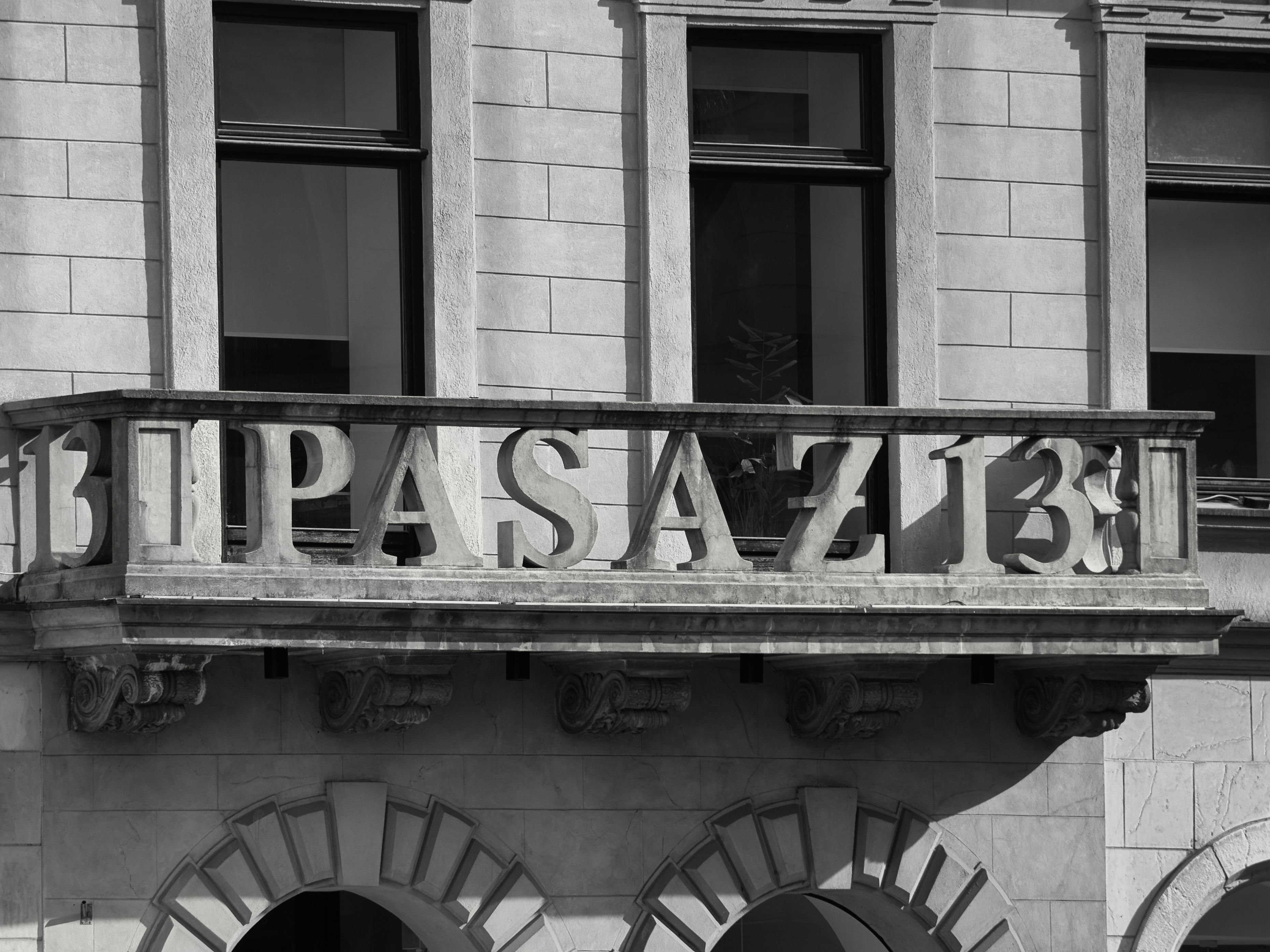 Black and white photo of a historic building facade with decorative stone elements and 'Pasaz 13' sign.
