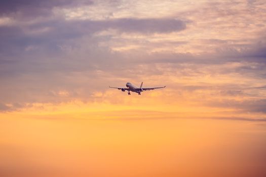 A passenger airplane flying against a vibrant sunset sky, creating a dramatic silhouette.