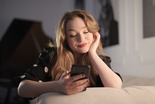 Free Smiling young woman enjoying leisure time on her smartphone in a cozy living room. Stock Photo