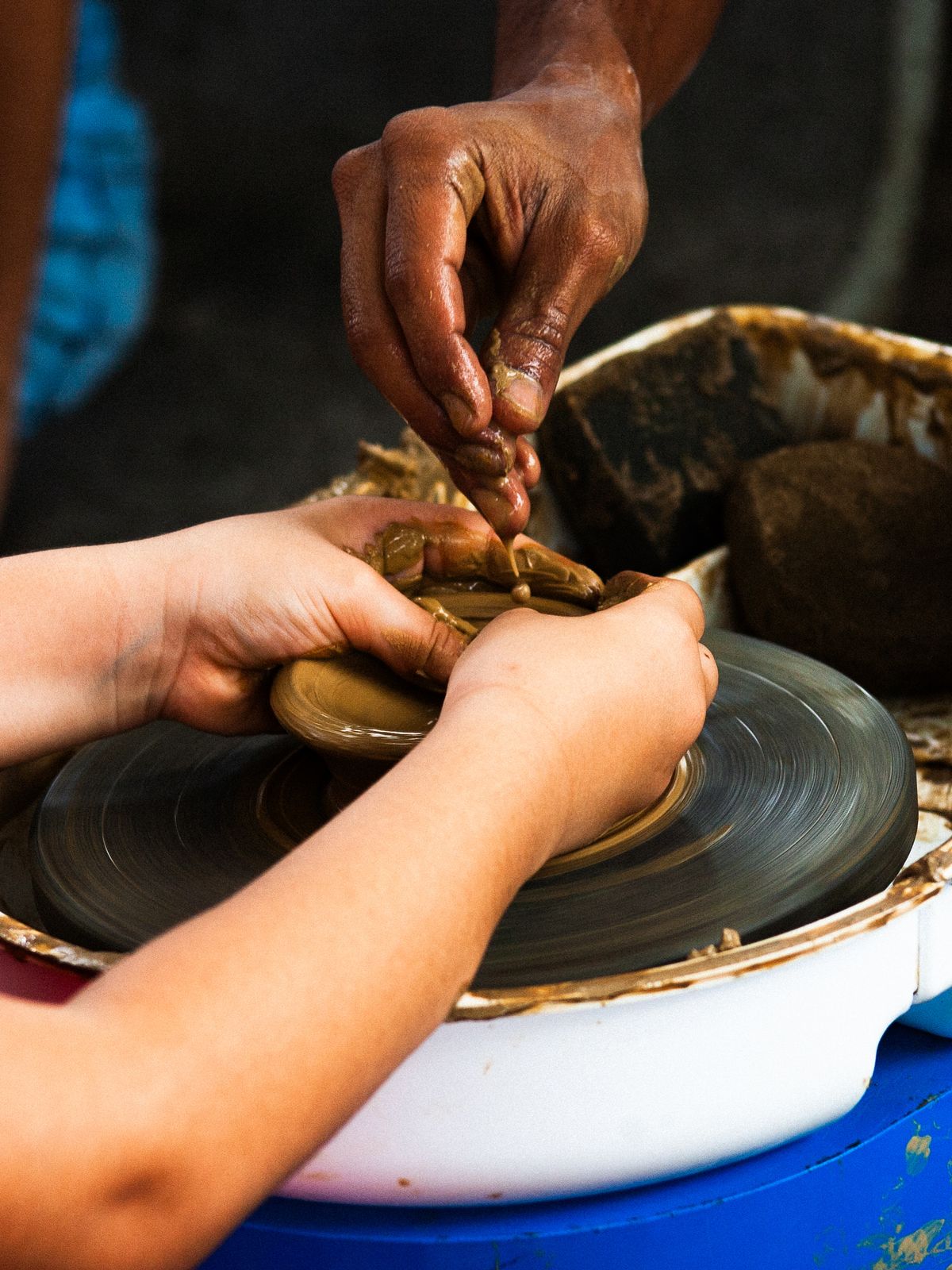 Two pairs of hands shaping clay together on a pottery wheel during a couples class