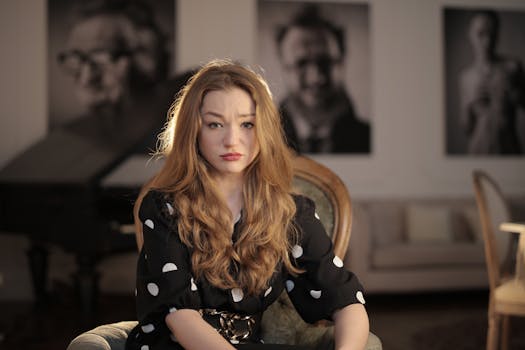 一位留着长波浪卷发的女子坐在室内，在模糊的背景前露出沉思的表情