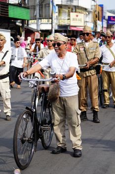 A group of adults in vintage uniforms participate in a bicycle parade on a city street. - Fotografer Sidoarjo