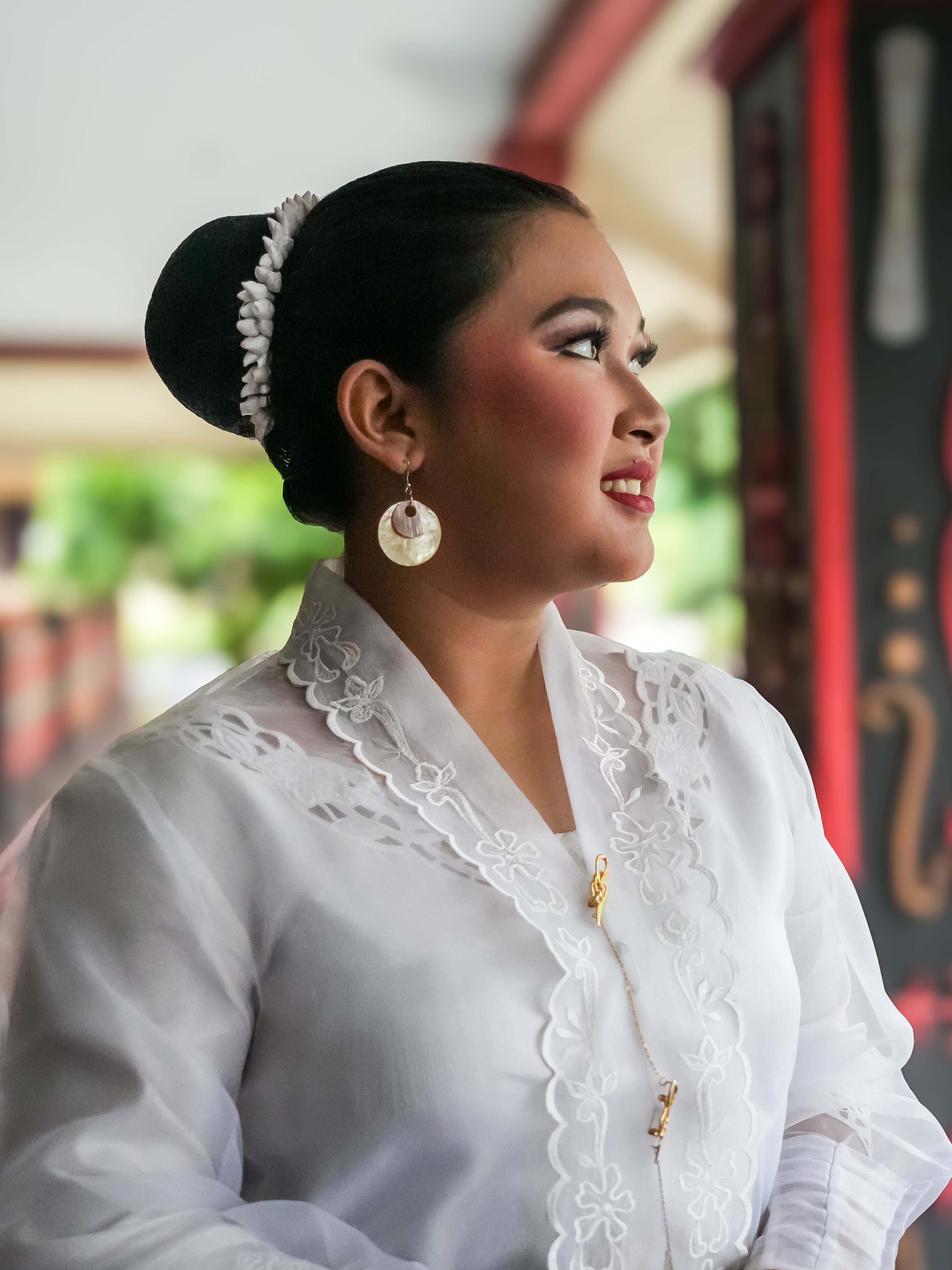 A woman in traditional white attire smiles gracefully while gazing outdoors.