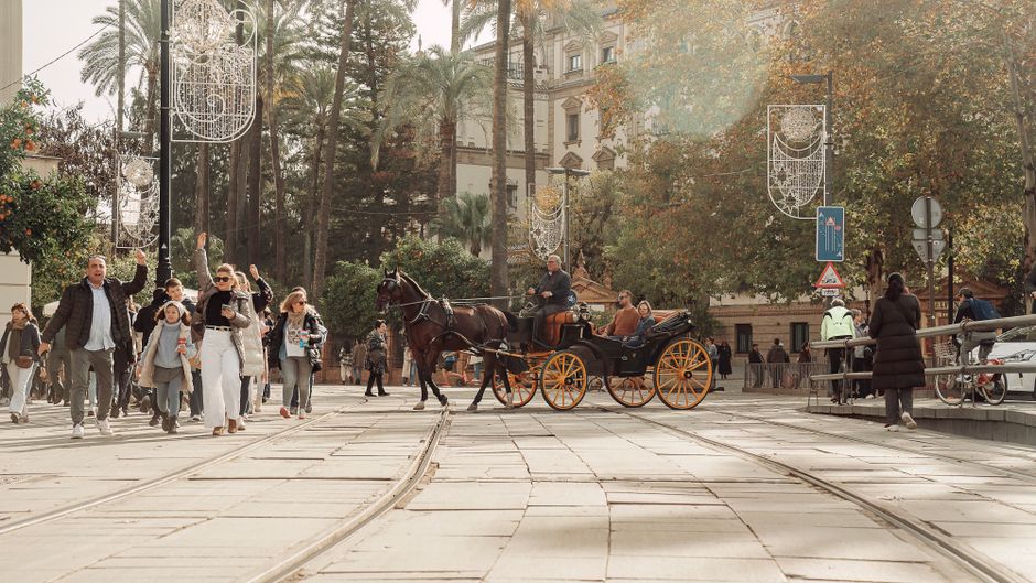 Personas disfrutan de un paseo en carruaje en un día soleado en Sevilla, España, mostrando la animada vida de la ciudad.