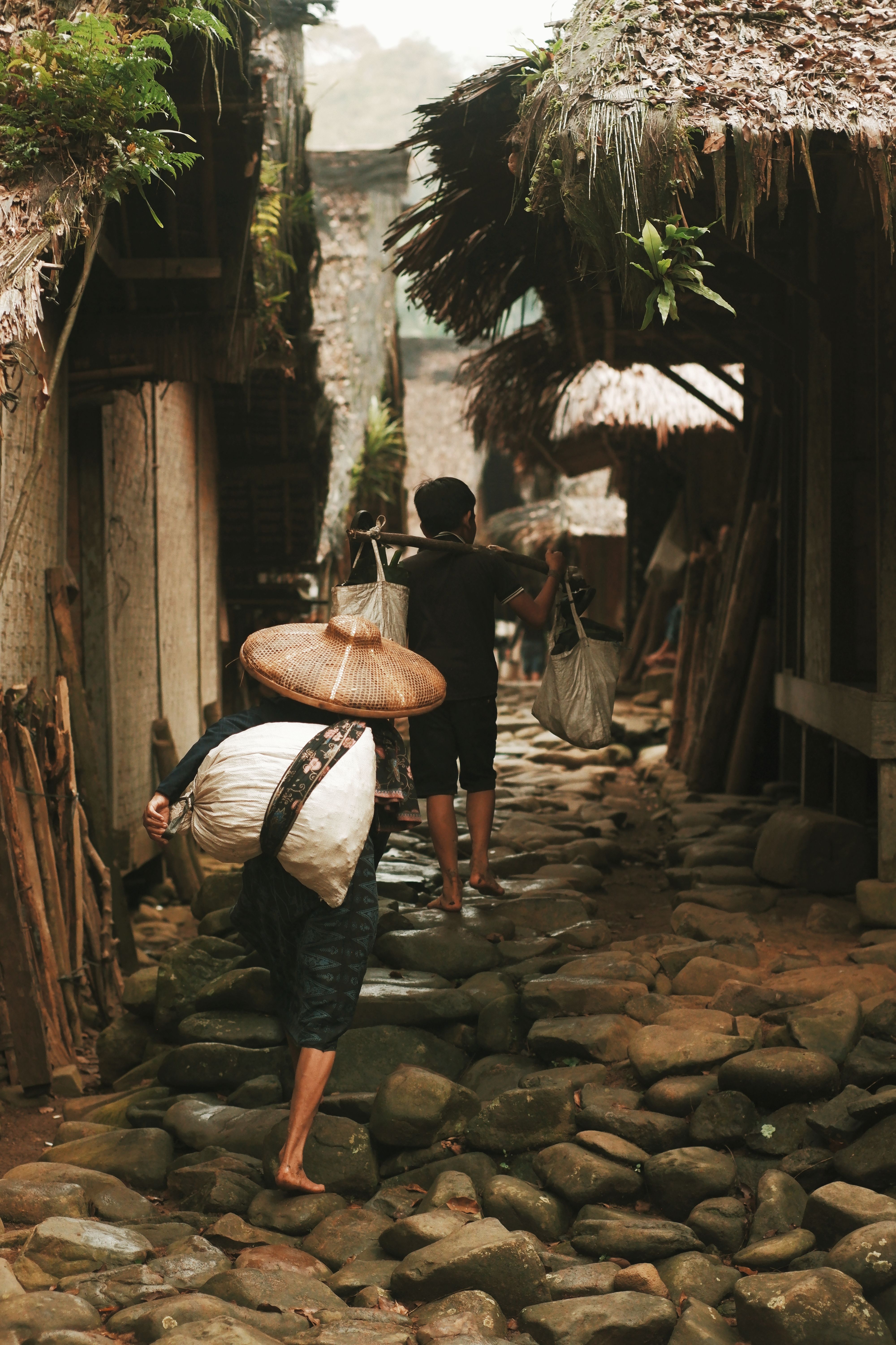 Villagers carrying goods along a cobblestone path in a traditional village in Banten, Indonesia.