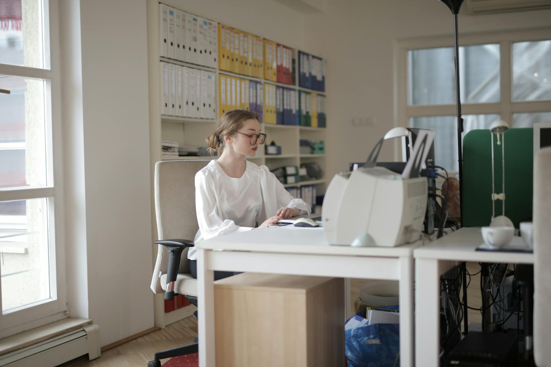 Focused woman working in a modern office filled with files and equipment.