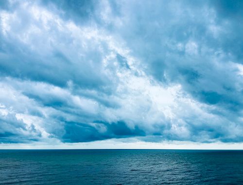 Free A breathtaking view of the ocean under a dramatic, cloud-filled sky, captured in soothing blue tones. Stock Photo