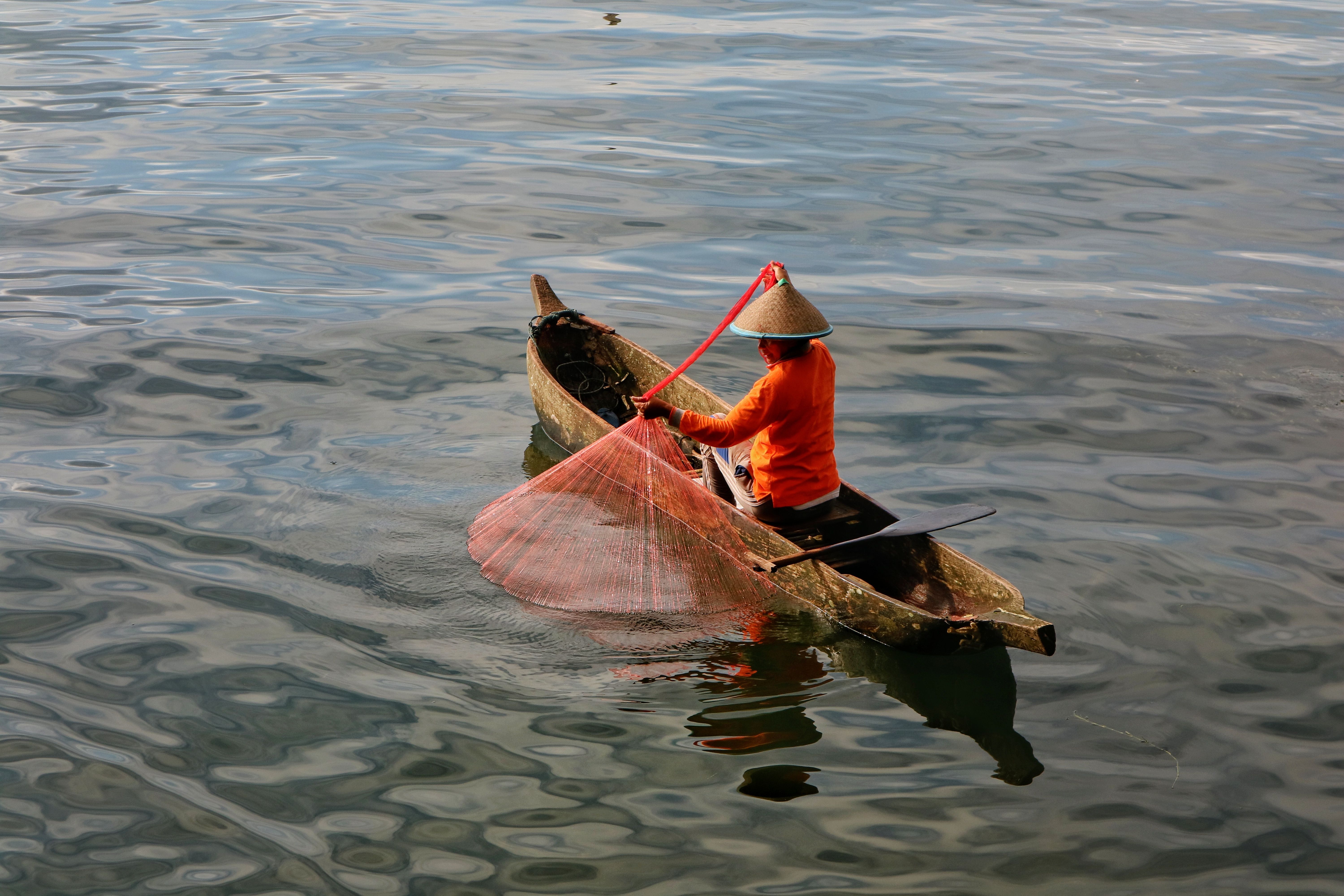 A local fisherman casts a net from a canoe on Lake Maninjau, West Sumatra, Indonesia.