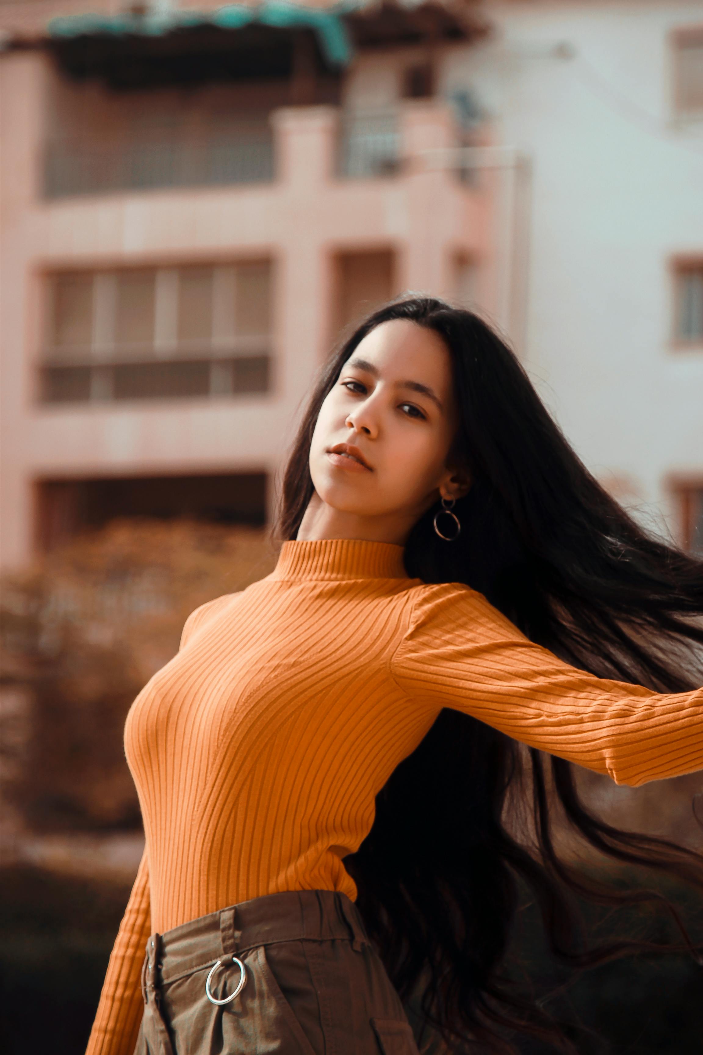 一位年轻女子穿着充满活力的橙色毛衣，在户外自信地摆出姿势，展现着时尚与优雅