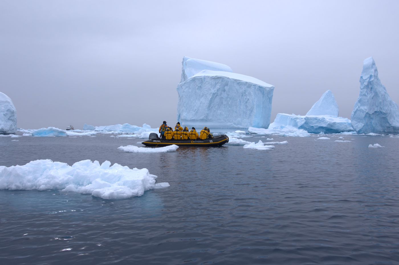 An expedition group in an inflatable boat moving through icy water beside large icebergs in Antarctica