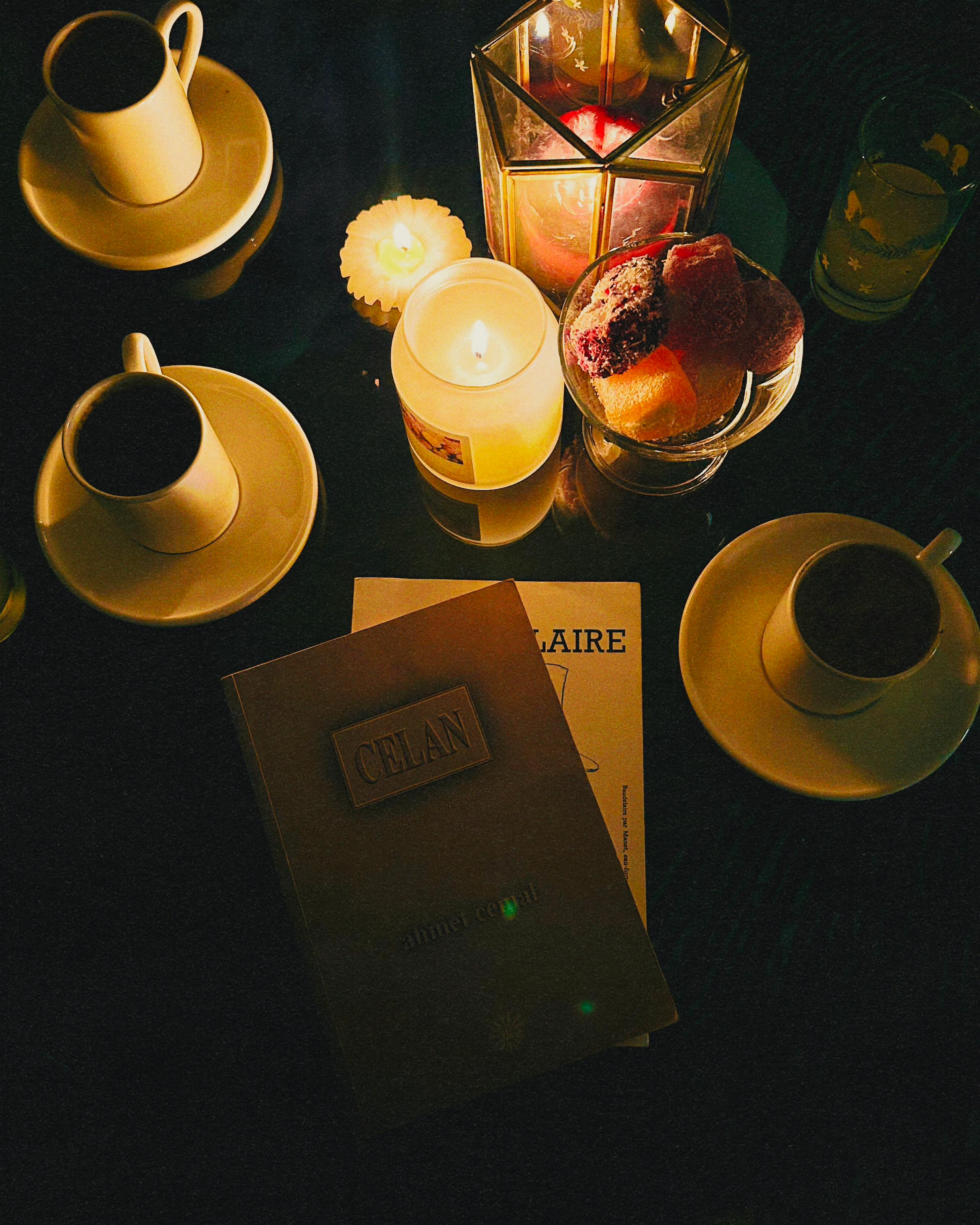 Candlelit table setting with coffee, books, and pastries, creating a warm, cozy atmosphere.