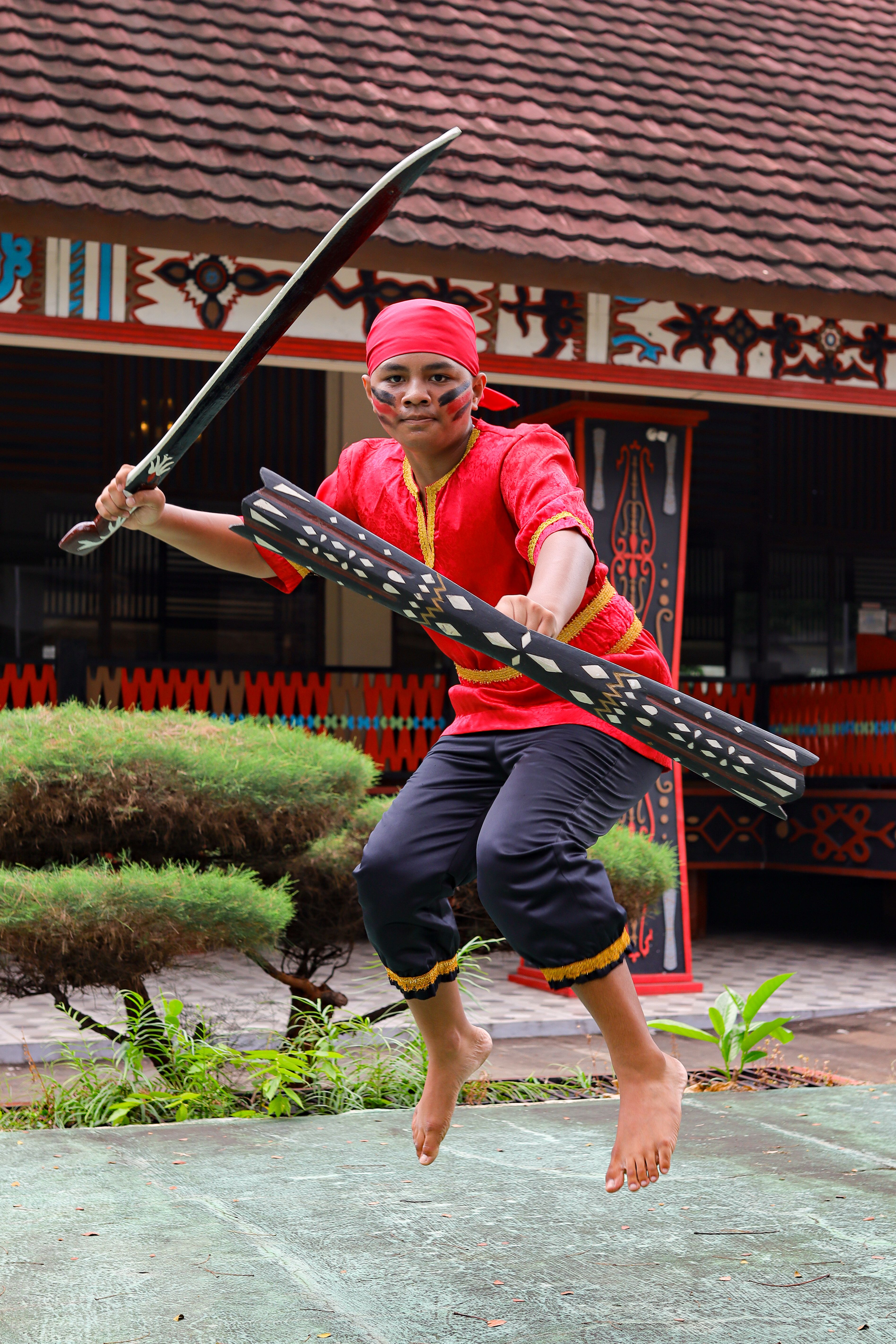 Energetic dancer performing in traditional Indonesian attire with sword and shield outdoors.