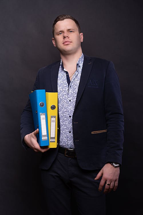 Man in Black Suit Holding Blue and Yellow Folders