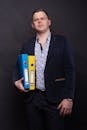 Man in Black Suit Holding Blue and Yellow Folders