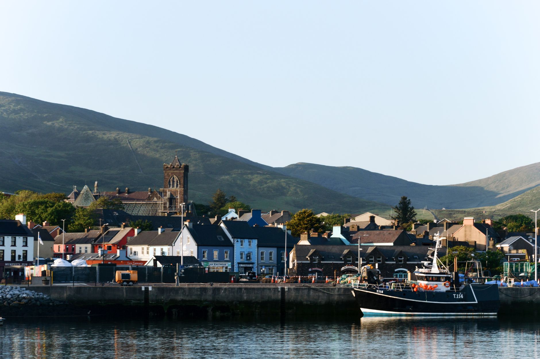 Beautiful coastal town of Dingle with fishing boat and church under hills.