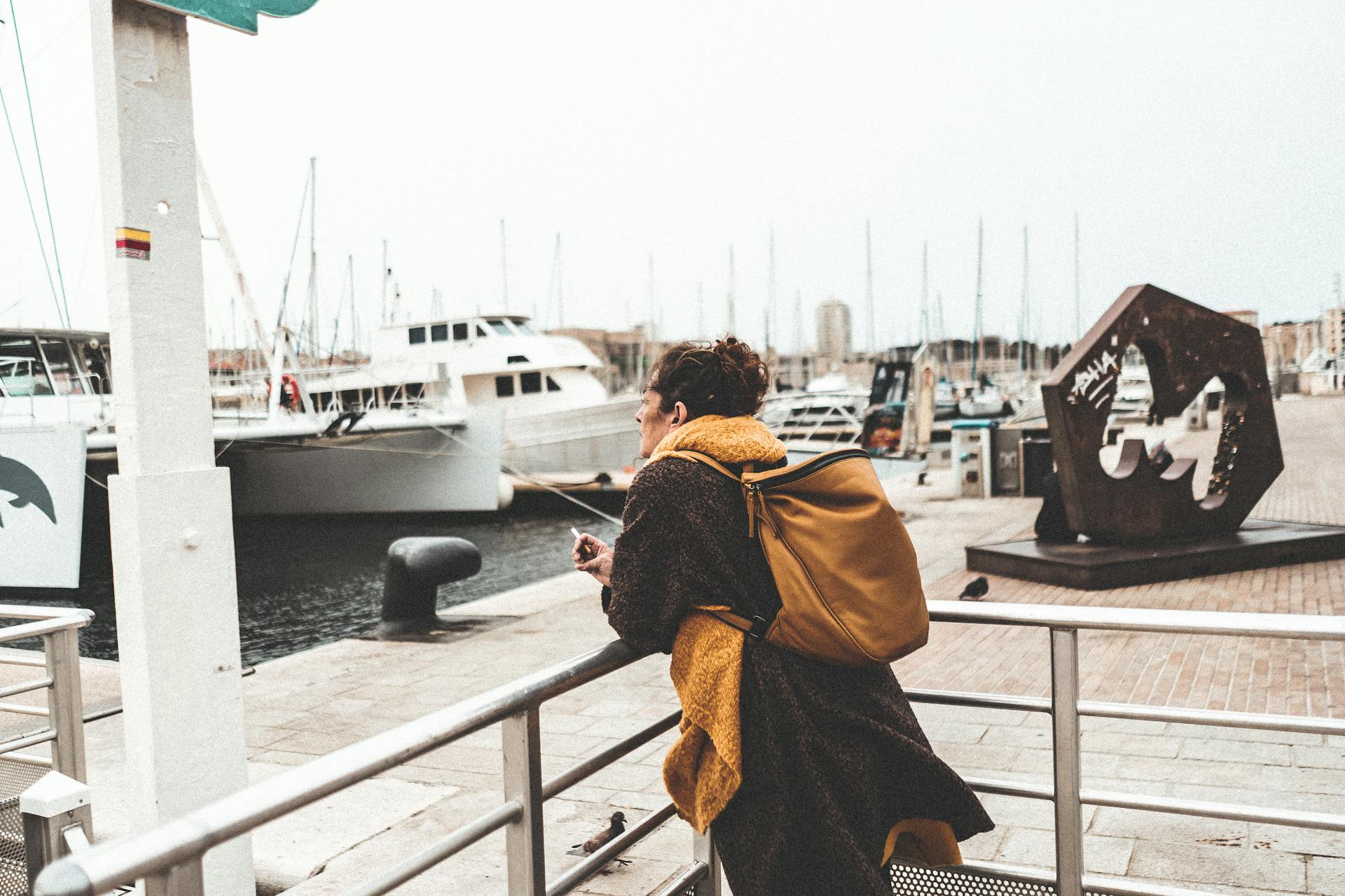 Woman with backpack gazing at sailboats in Marseille harbor, Provence-Alpes-Côte d'Azur, France.