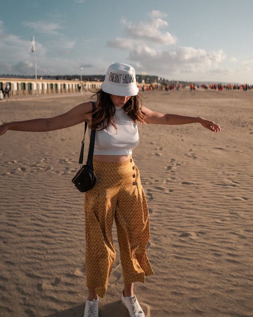 Woman in White Tank Top and Brown Pants Standing on Brown Sand