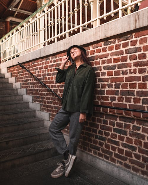 Woman in Green Long Sleeve Leaning on Brick Wall Beside Concrete Stairs