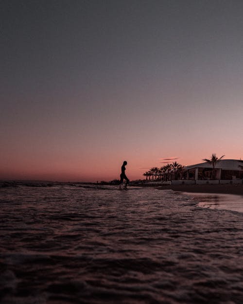 Silhouette of Woman Walking on Beach during Sunset