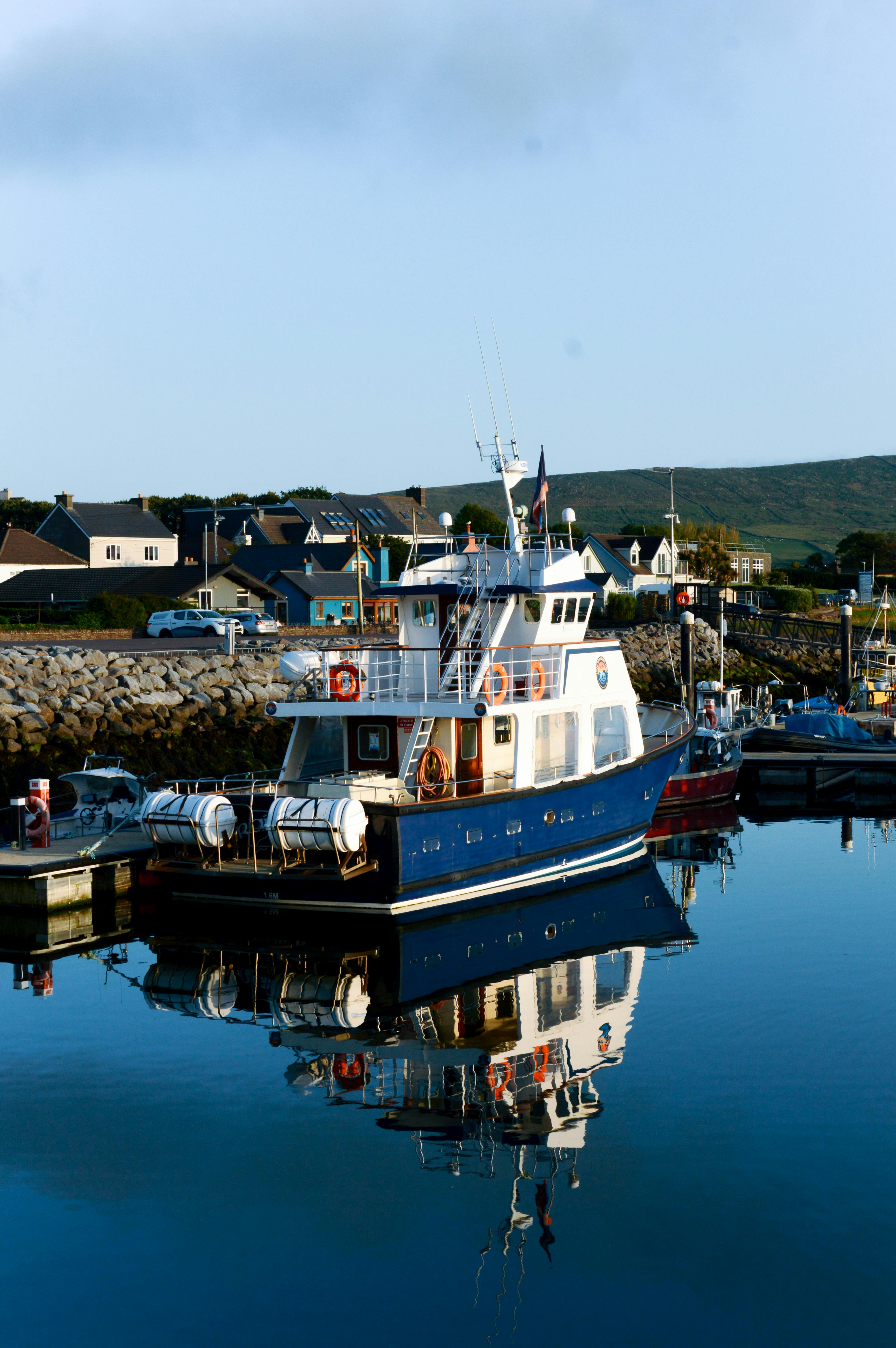 Serene morning view of boats reflected in the calm waters of Dingle Harbor, Ireland.