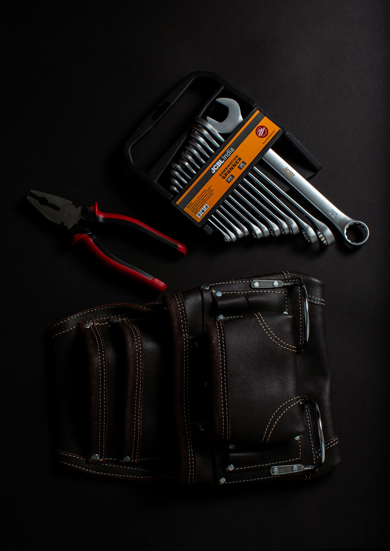 A mobile mechanic's spanner set, pliers and leather tool pouch laid out on a dark surface