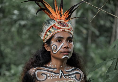 Free A woman in tribal attire with face paint amid a lush forest setting. Stock Photo