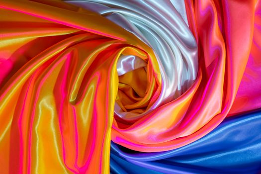 Bright swirling satin fabrics showcasing vivid neon colors and iridescent textures in an abstract composition.