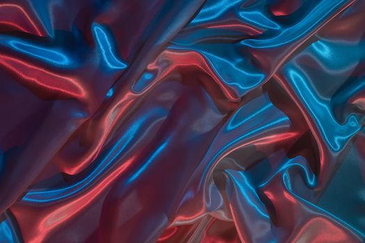 Close-up of vibrant blue and red satin fabric with a neon-lit, flowing texture.