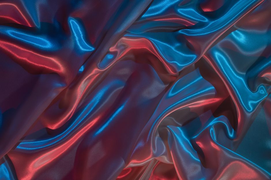 Close-up of vibrant blue and red satin fabric with a neon-lit, flowing texture.