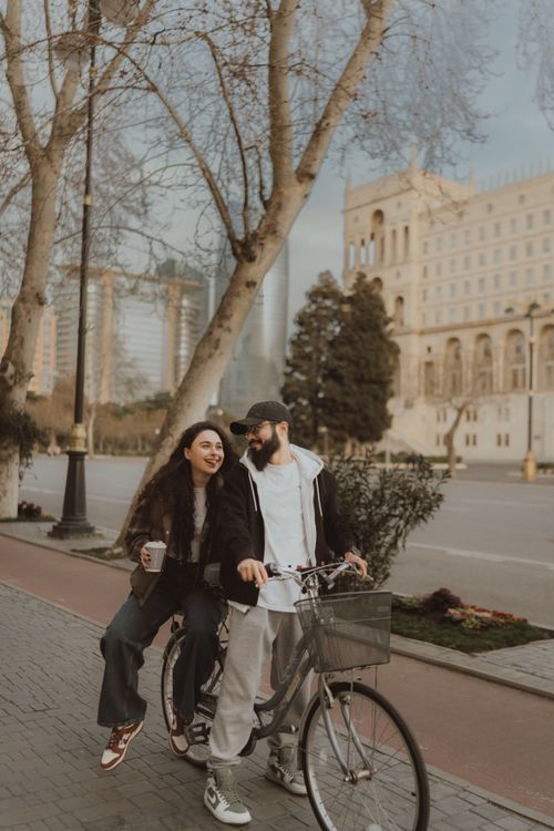 Free A couple shares a joyful moment on a bicycle ride through a city street, capturing a charming urban scene. Stock Photo