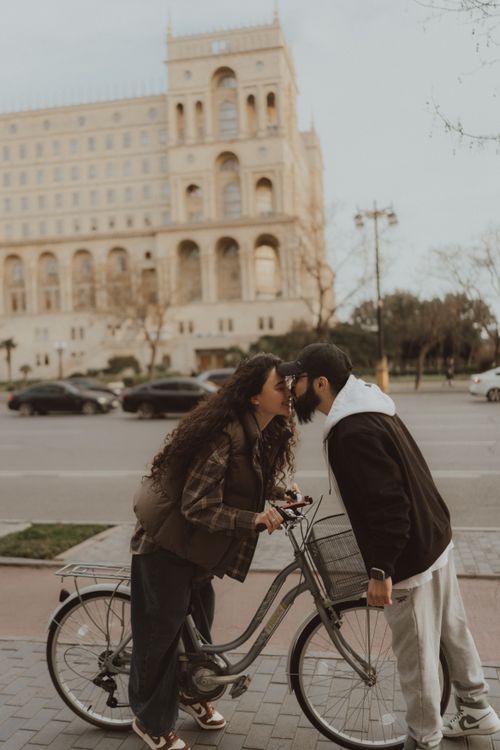 Free Couple sharing a kiss by a bike in front of a historical building in an urban setting. Stock Photo