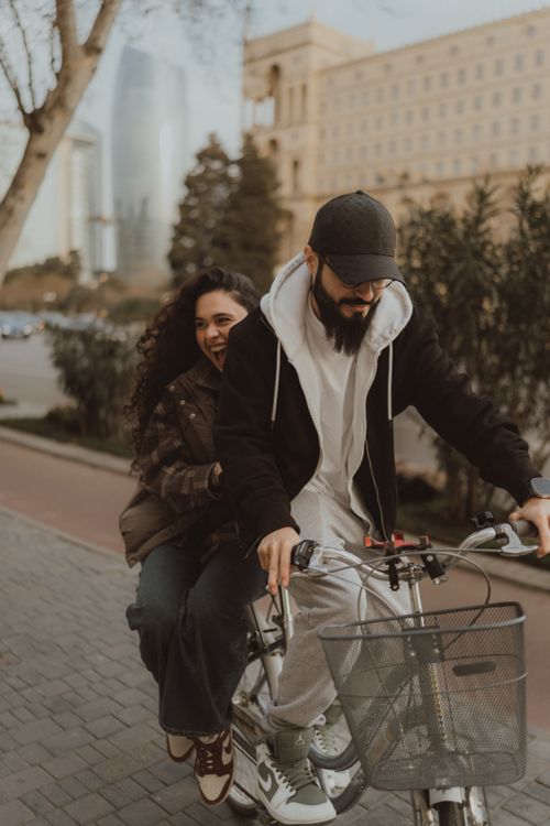 Free Smiling couple riding a bicycle together in a city environment. Urban adventure and joy. Stock Photo