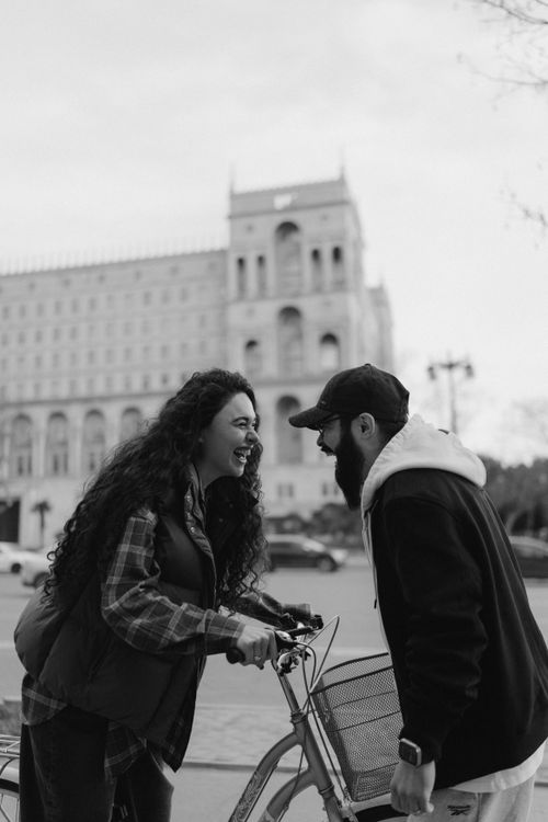 Free Black and white photo of a laughing couple enjoying a moment with a bicycle in a city setting. Stock Photo