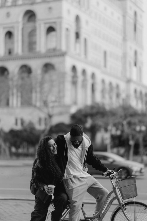 Free A happy couple shares a laugh while resting on a bicycle in an urban setting. Stock Photo