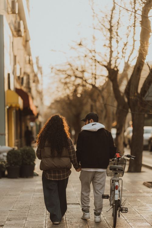 Free Young couple strolling hand in hand with a bike on a sunlit city street. Stock Photo