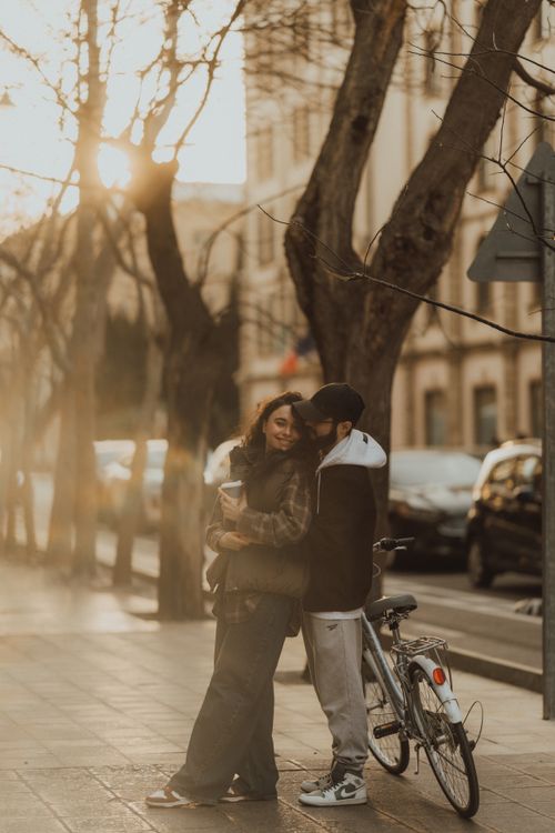 Free A couple shares a tender moment by a bicycle on a sunlit city street, evoking romance and warmth. Stock Photo