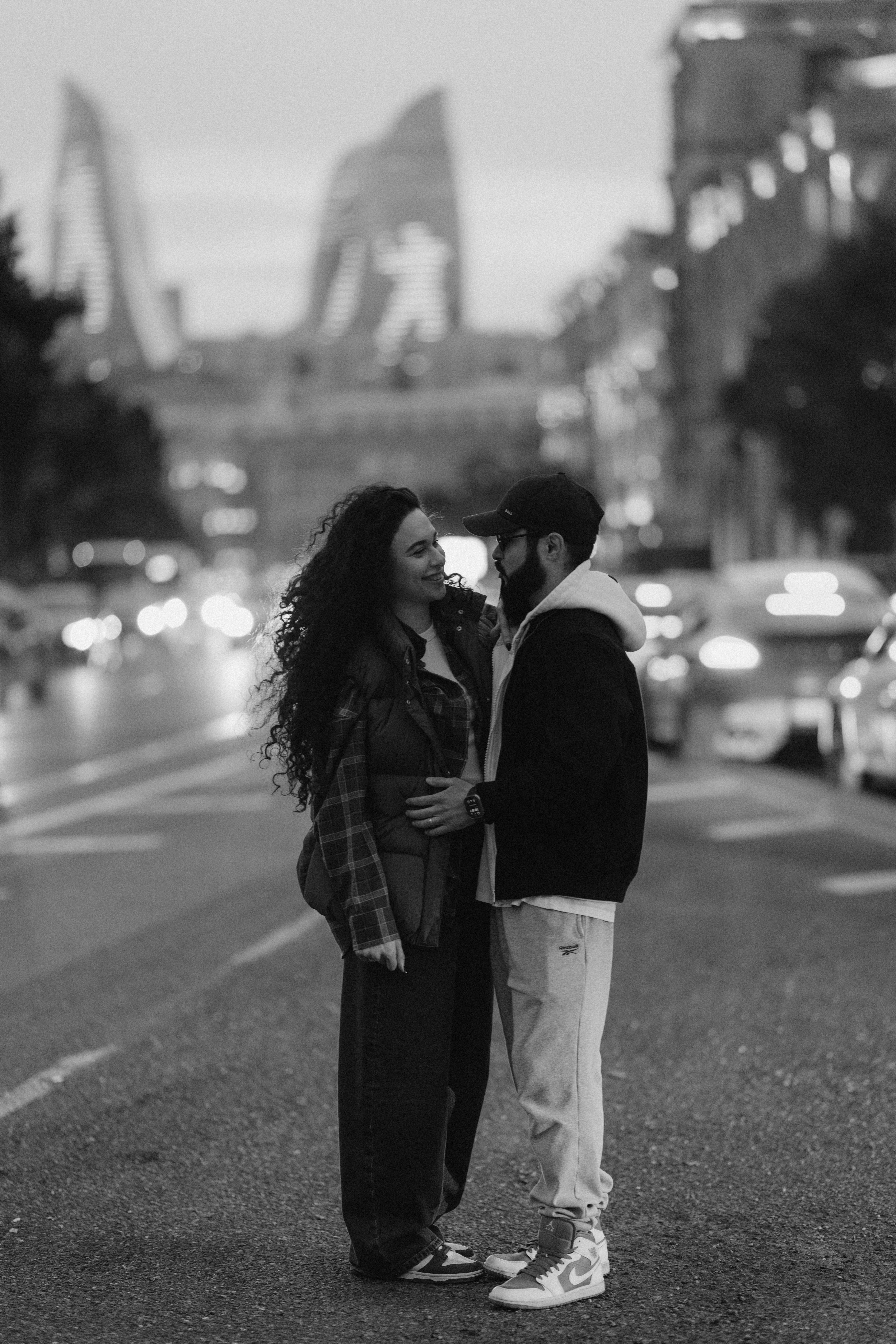 Black and white photo of a couple standing on a city street with blurred lights behind them.