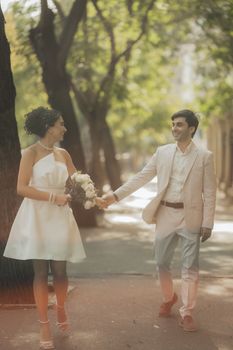 A joyful couple walks hand in hand during their outdoor wedding ceremony with lush greenery around.