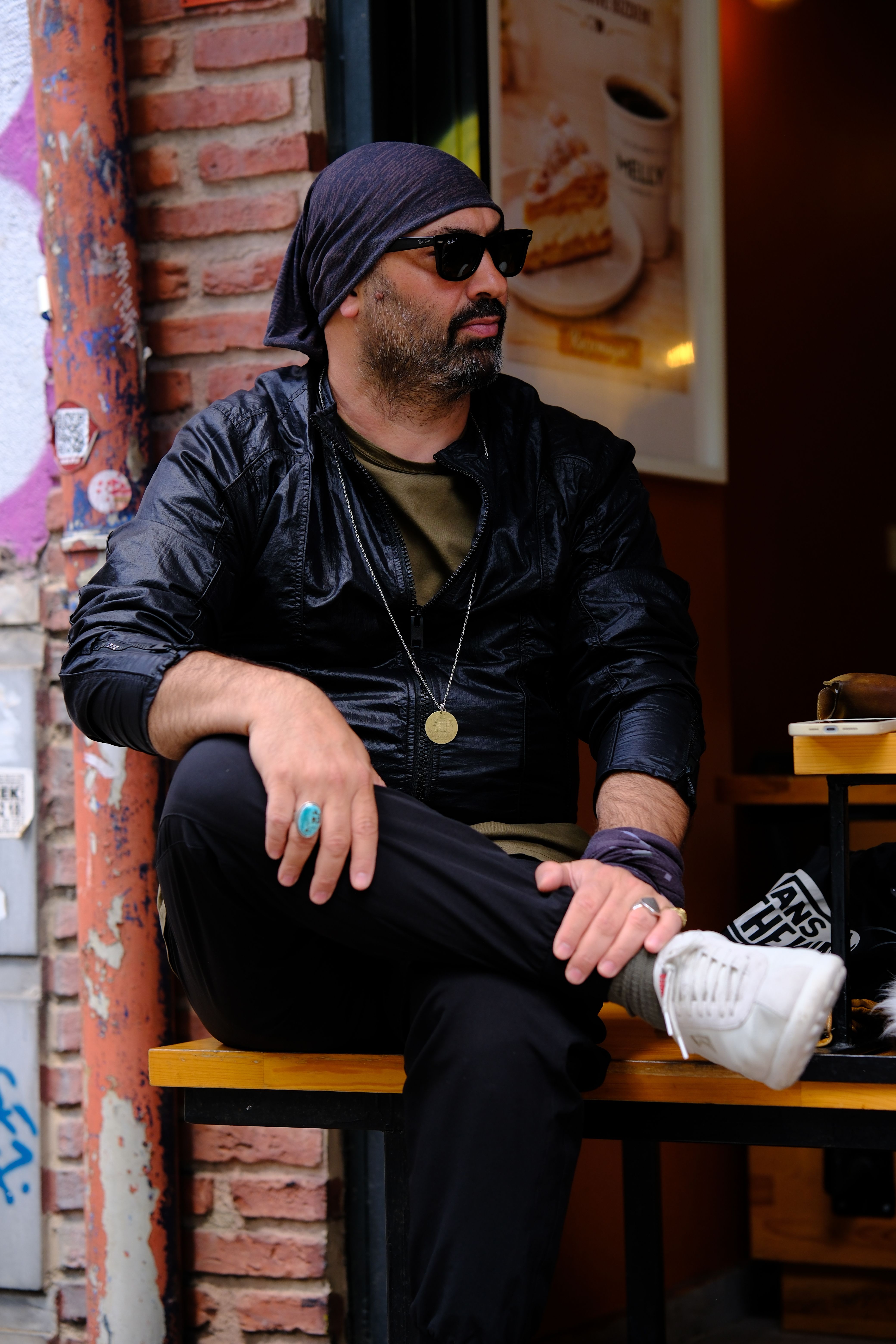 Stylish man with beard and sunglasses sitting outdoors at a café.
