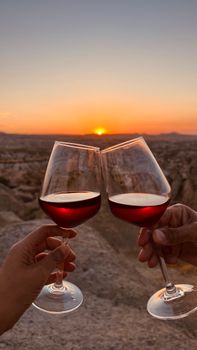 Two wine glasses clinking at sunset outdoors, celebrating nature's beauty.